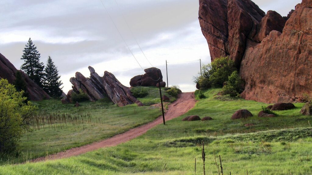 Red rock formations with winding dirt path lush grass and stones under a peaceful sky wallpaper