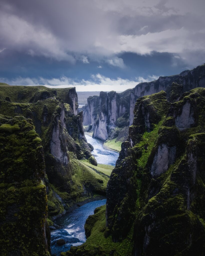 Dramatic river winding through steep cliffs mossy rocks lush green foliage under moody sky wallpaper