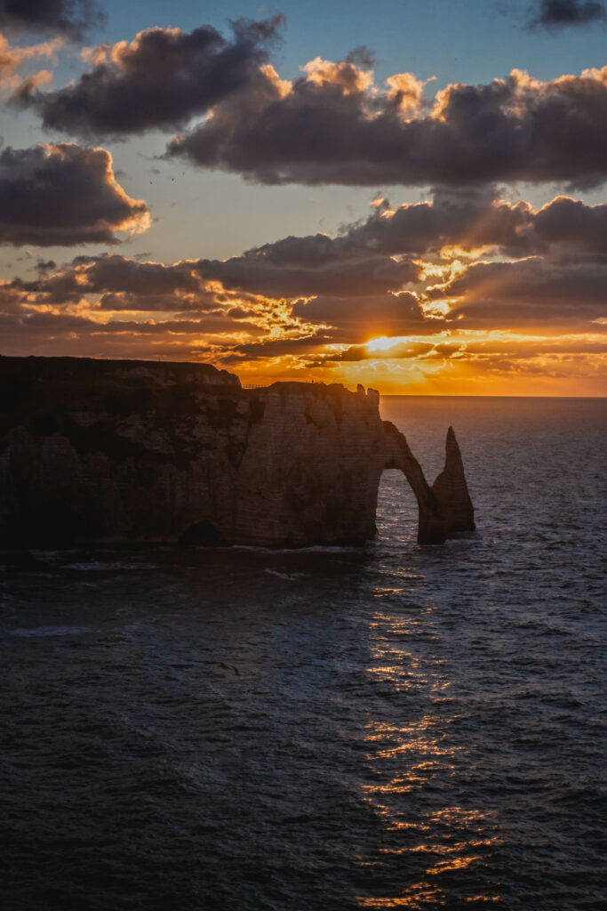 Dramatic coastal rock arch with crashing waves under vibrant golden orange sunset sky wallpaper
