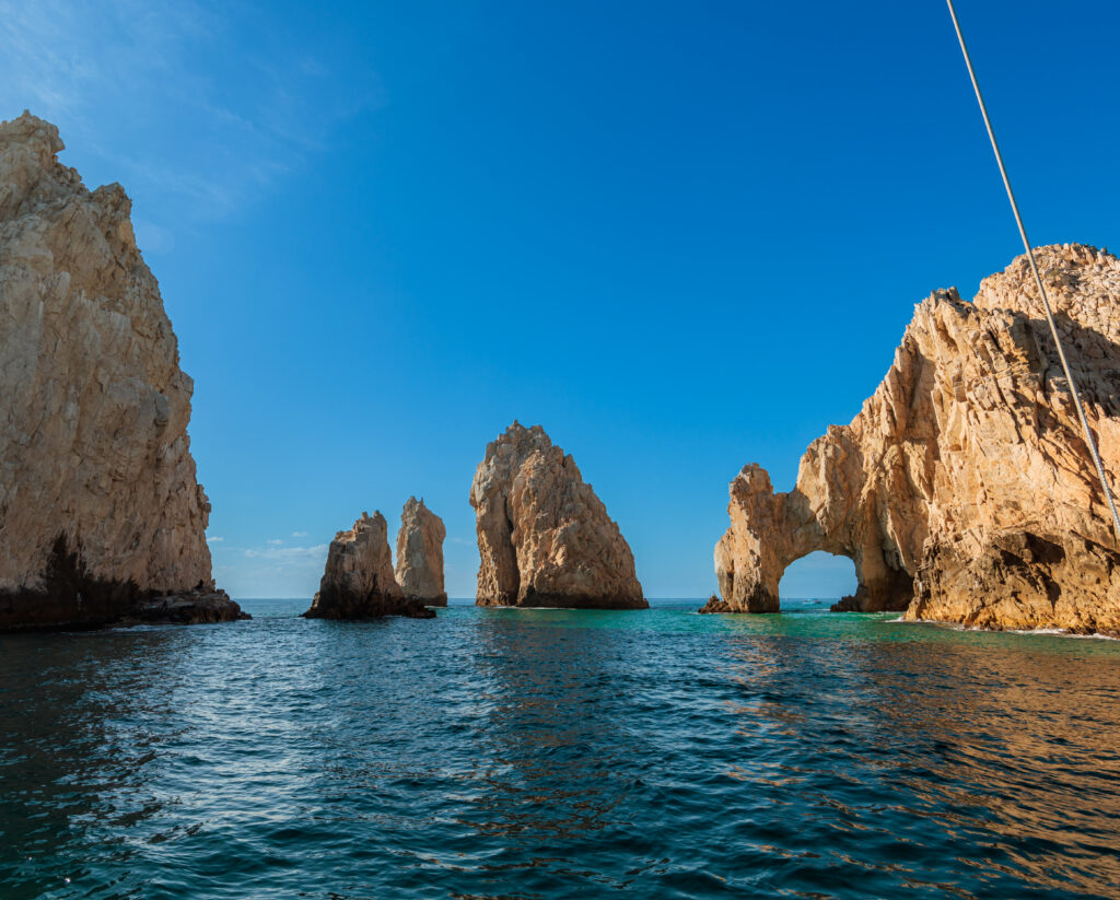 Dramatic rock formations with natural arch rising from calm sea under deep blue sky wallpaper background