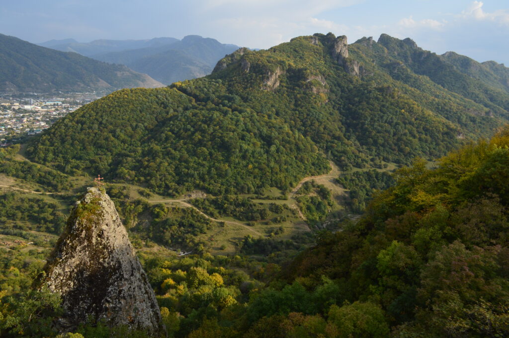 Dramatic rock peak overlooking lush green valley rolling hills and distant mountains landscape wallpaper