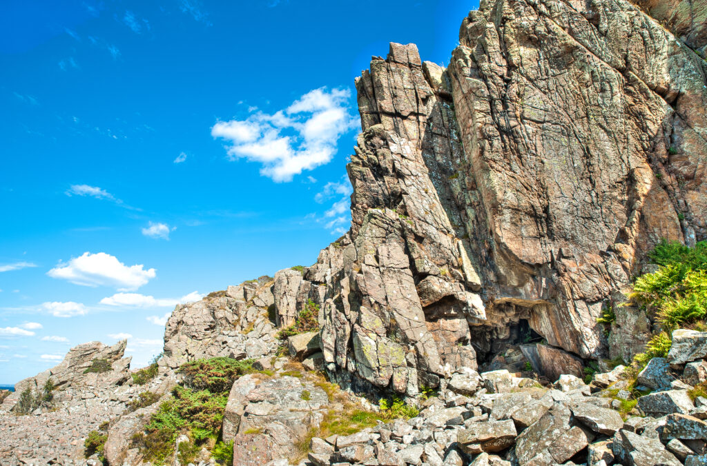 Dramatic rock relief with rugged stones and greenery under vibrant blue sky outdoor wallpaper background
