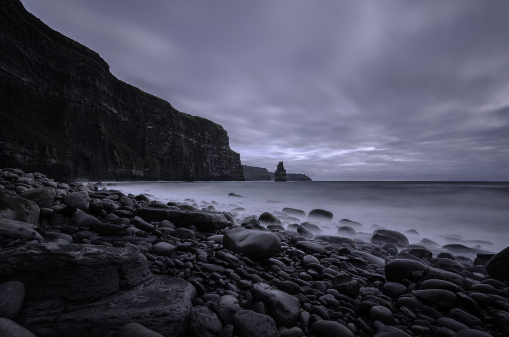 Dramatic rocky beach with smooth stones misty sea moody sky steep cliffs serene water wallpaper