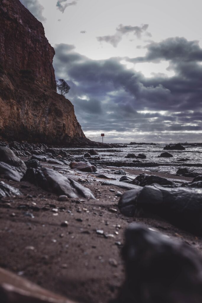 Dramatic coastal wallpaper with dark rocks shore rugged cliff and moody cloudy sky over calm sea