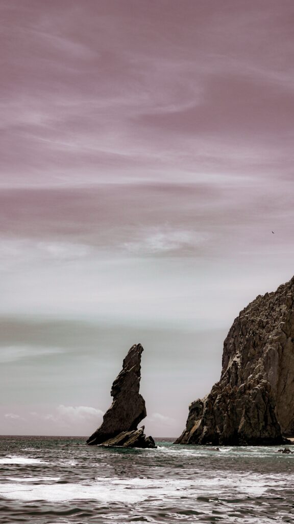 Dramatic rocky cliffs and jagged sea stacks over wavy ocean waters under pastel sky wallpaper background