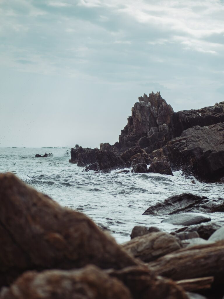 Dramatic rocky cliffs and ocean waves crashing under cloudy sky rugged coastline wallpaper background