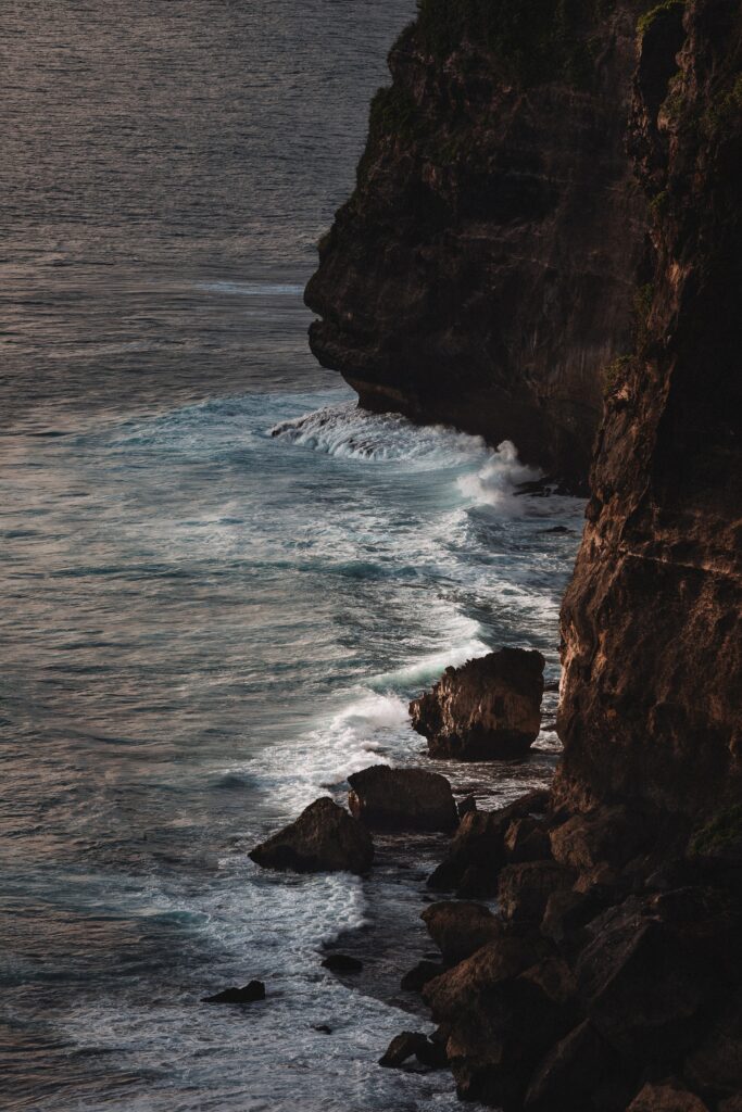 Dramatic rocky cliffs meet crashing waves in serene evening light coastal wallpaper background
