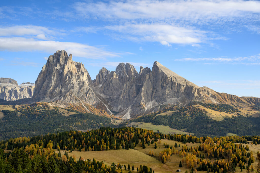 Rocky mountain peaks above lush green valley with golden autumn trees under blue sky clouds Wallpaper