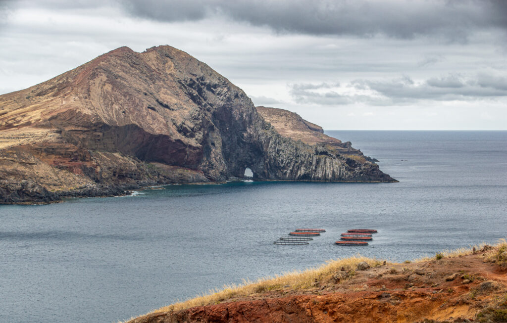 Dramatic rocky mountain and rugged coastline with earthy tones by calm blue sea and cloudy sky Wallpaper