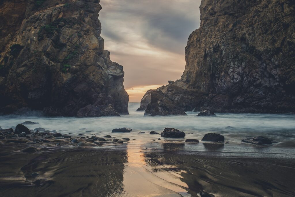 Dramatic rocky shoreline at sunset with crashing waves and smooth stones wallpaper background