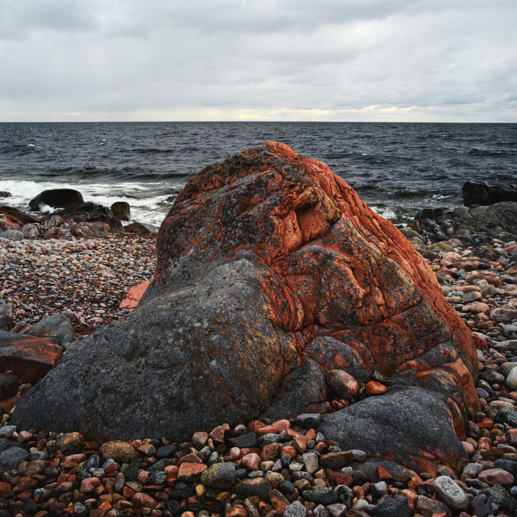 Dramatic rocky shoreline with weathered stone and multicolored pebbles under cloudy sky Wallpaper