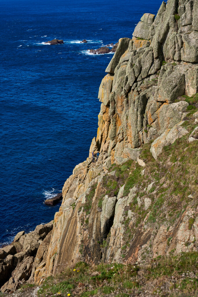 Rugged weathered cliff overlooking deep blue sea with crashing waves and wild coastal grass wallpaper