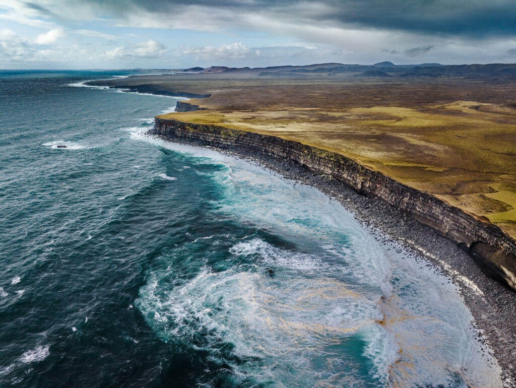 Rugged coastline with dramatic cliffs and swirling sea waves under dynamic cloudy sky wallpaper