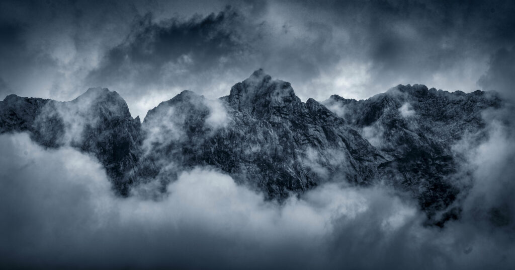 Dramatic rugged mountain peaks shrouded in swirling clouds with dark moody rocky textures wallpaper