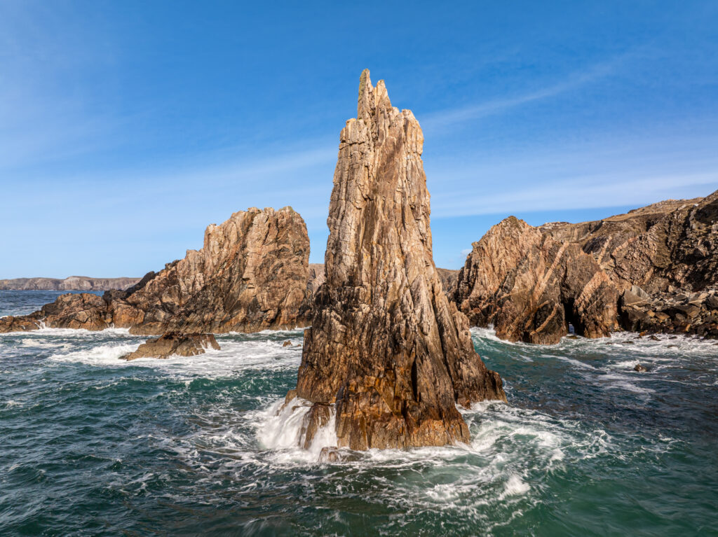 Rugged mountain rock formations rise from crashing foamy waves under vibrant blue coastal sky wallpaper