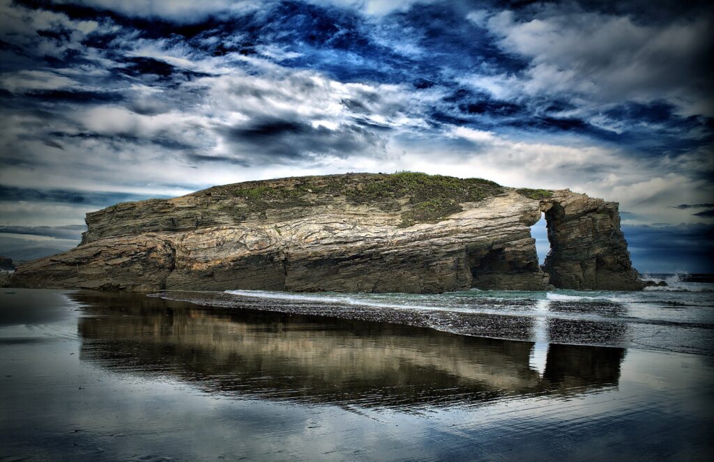 Dramatic seascape with rugged rock formation and moody blue gray sky reflected in shallow water Wallpaper
