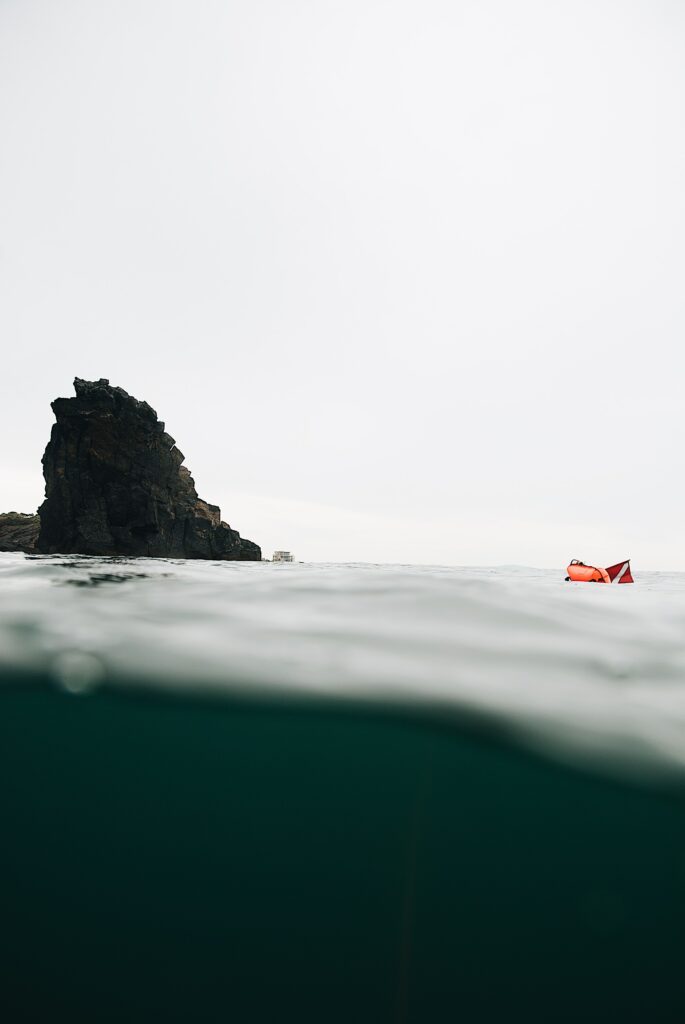Dramatic seascape wallpaper with rugged rock formation calm gray waters and vibrant orange float
