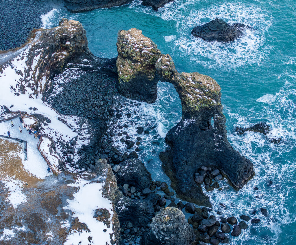 Aerial view of sea arch with rugged rocks snow-tipped coast and vibrant blue ocean waters wallpaper