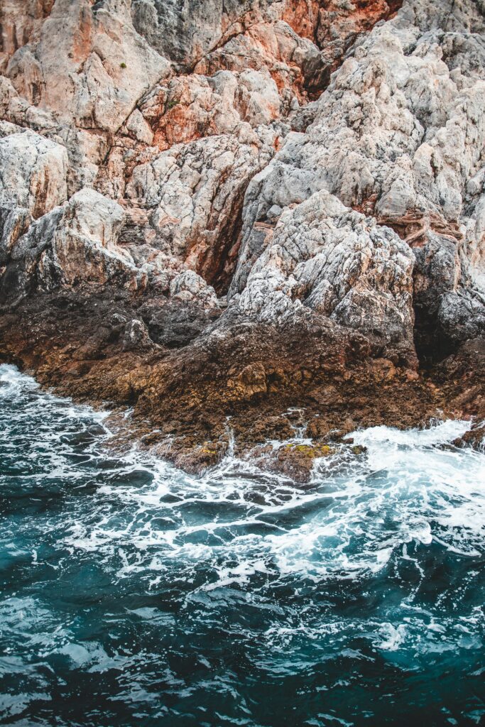 Dramatic sea waves crashing rugged coastal rocks with rich textures and deep blue water background Wallpaper