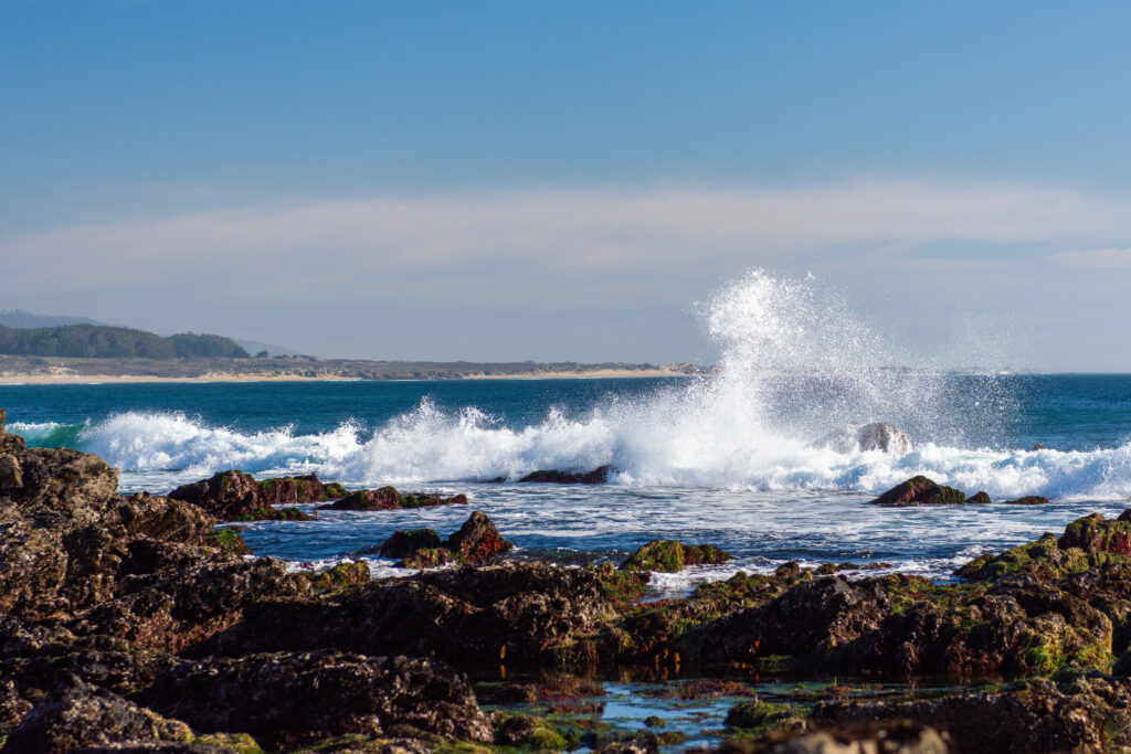 Powerful sea waves crash on rugged rocky shore under clear blue sky vibrant nature wallpaper
