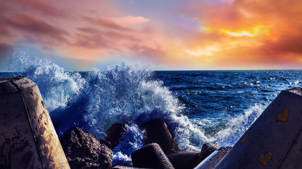 Dramatic sea waves crashing on rugged rocks under vibrant orange and pink sunset sky wallpaper