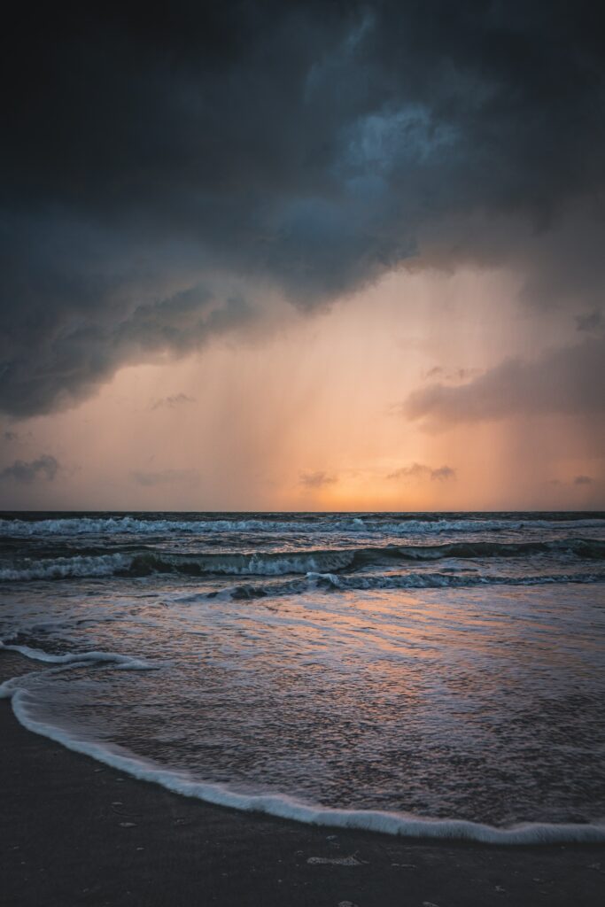 Dramatic sunset seascape with storm clouds golden light reflecting on wet sand waves Wallpaper