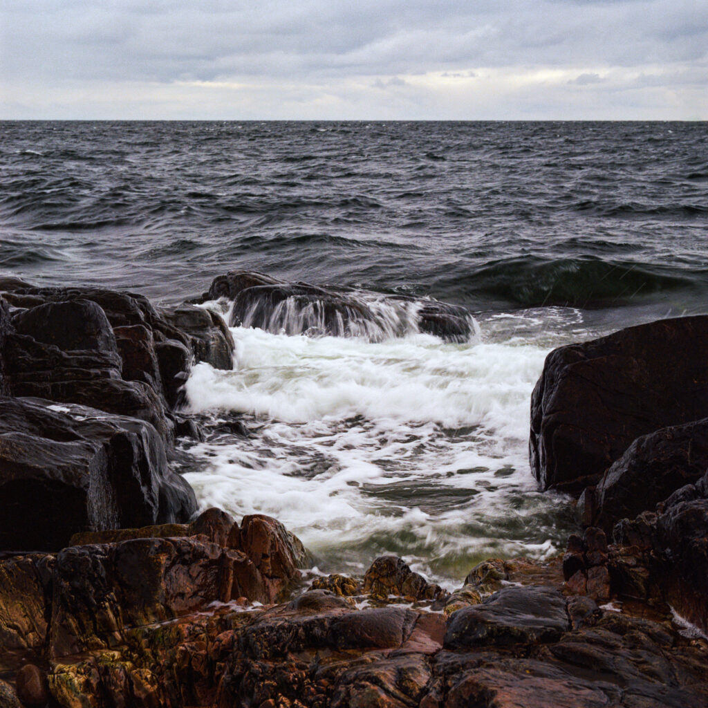 Dramatic seascape with foamy waves crashing rugged stones under cloudy sky wallpaper background