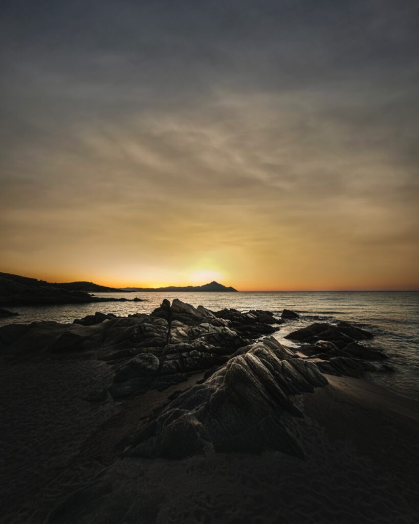 Dramatic seascape with rugged rocks sandy beach ocean waves golden sunset moody sky wallpaper