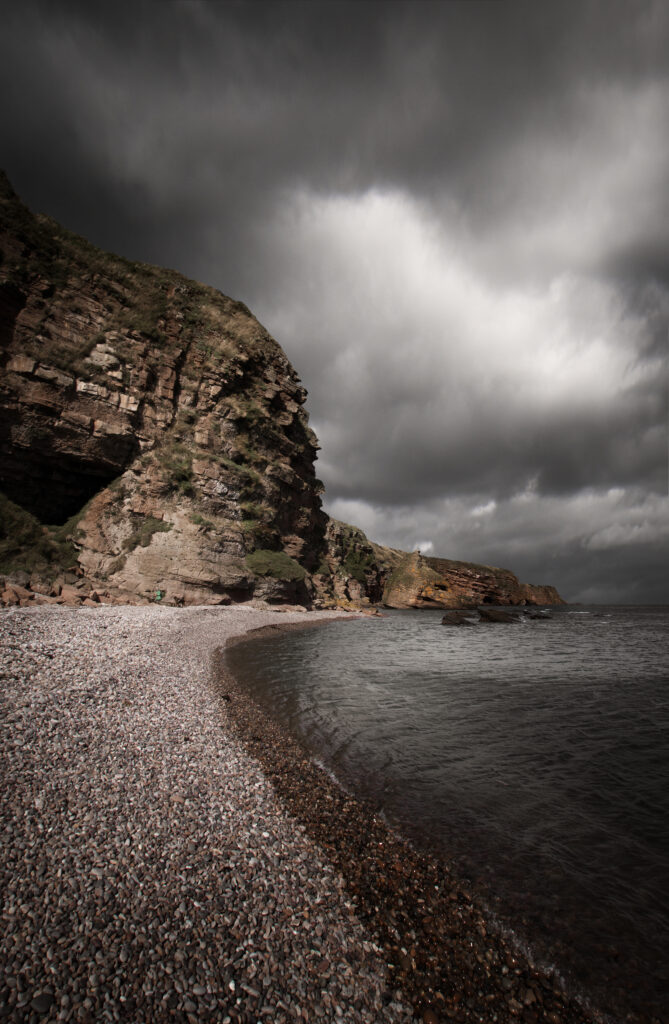 Dramatic seascape with pebble shore cliffs dark moody clouds calm sea natural textures wallpaper