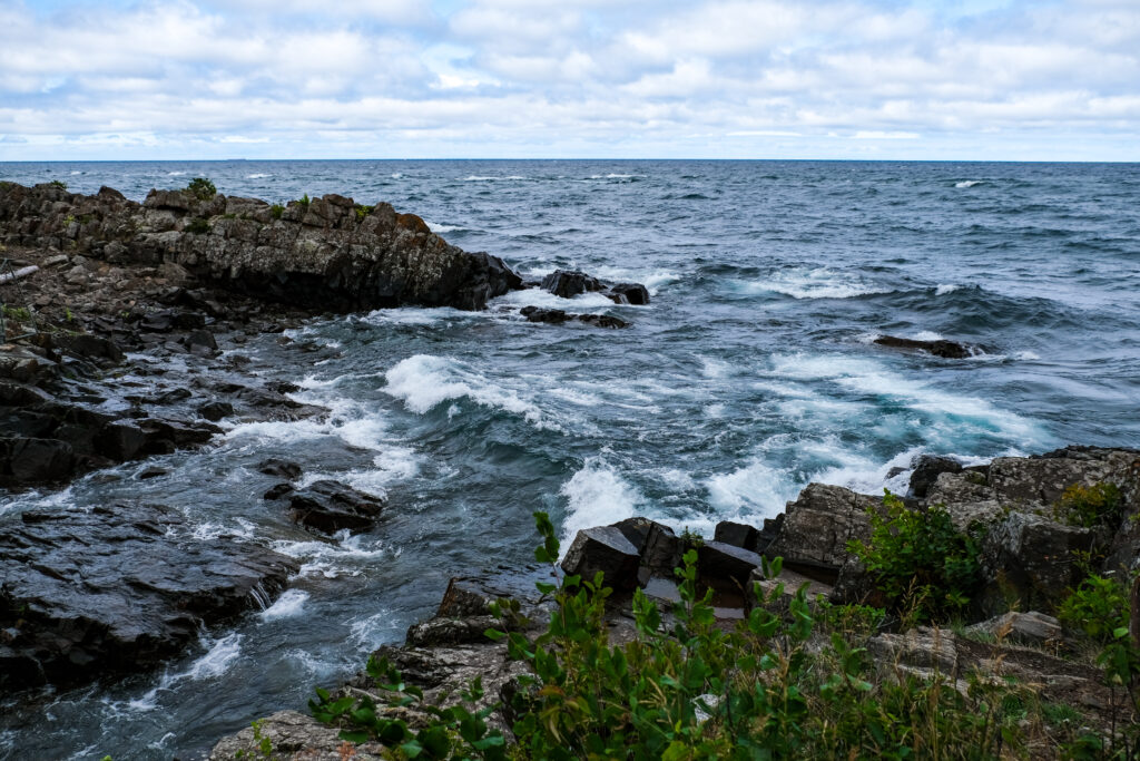 Dramatic seascape wallpaper with crashing waves on rugged rocks under soft cloudy sky