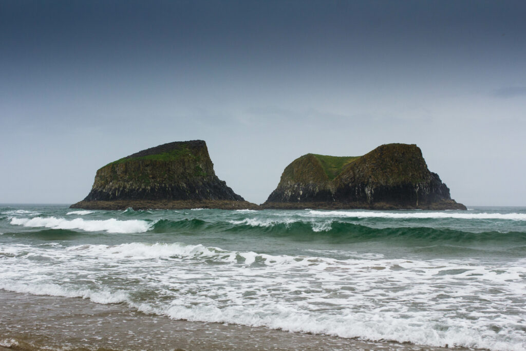 Dramatic seascape with rocky formations crashing waves sandy shore moody overcast sky wallpaper