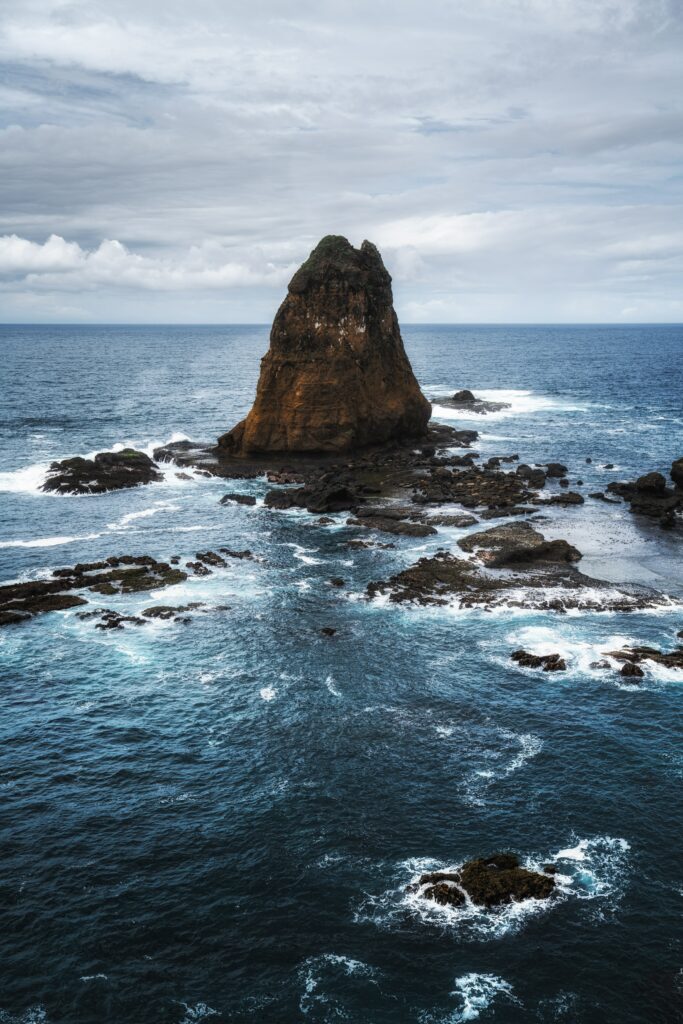 Dramatic seascape with rugged rock formation and foamy waves under moody cloudy sky wallpaper