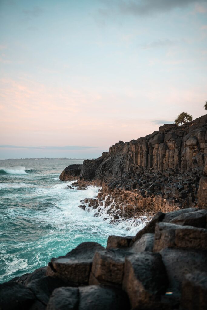 Dramatic seascape with rugged rocks geometric stone formations crashing waves pastel sky wallpaper