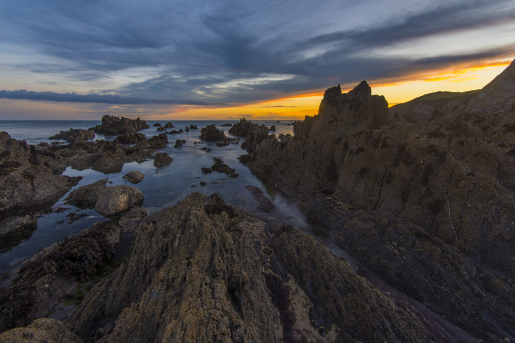 Dramatic rugged rocky shoreline with gentle waves and vivid sunset sky coastal seascape wallpaper