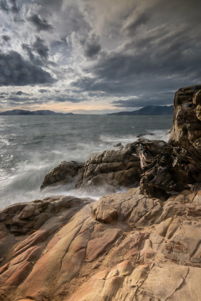 Dramatic rugged rocky shoreline with crashing waves and cloudy sky in muted earth tones wallpaper