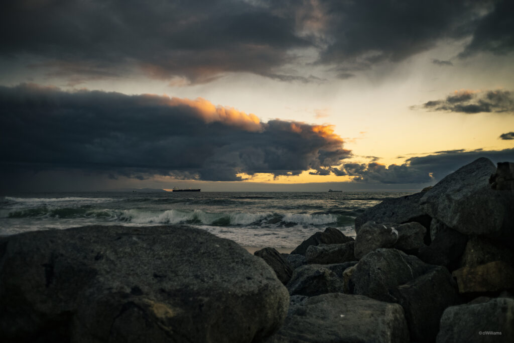 Dramatic seascape wallpaper with rugged rocks crashing waves moody sunset sky background