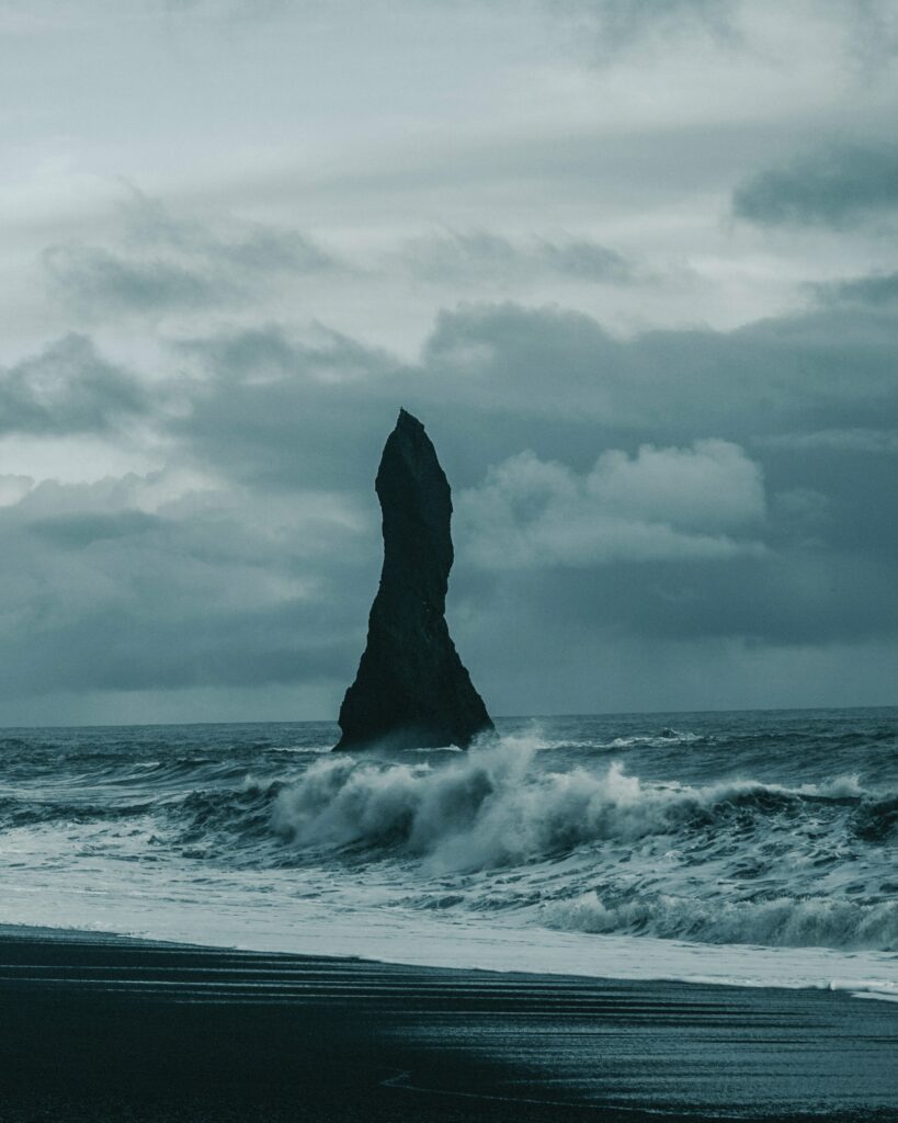 Dramatic seascape with towering rock formation and turbulent waves under cloudy sky wallpaper background