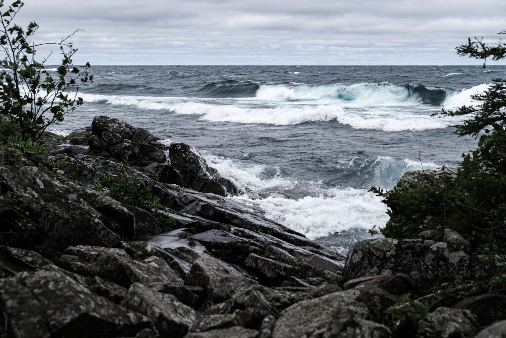 Dramatic seascape with crashing waves and rocky shore under cloudy sky in cool muted tones Wallpaper