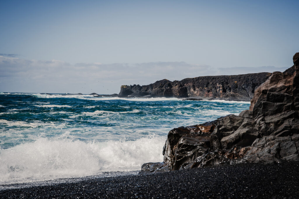 Dramatic seascape with powerful waves crashing dark rugged rocks under clear blue sky wallpaper