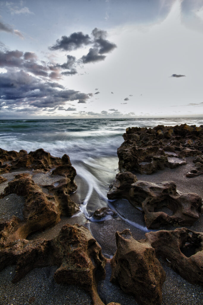 Dramatic seashore with rugged rocks foamy waves and moody cloud-filled sky coastal wallpaper