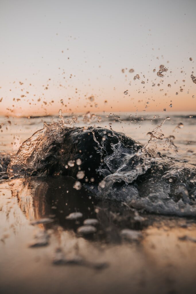 Dramatic seaside splash with crystal-clear water droplets frozen midair at golden sunset Wallpaper