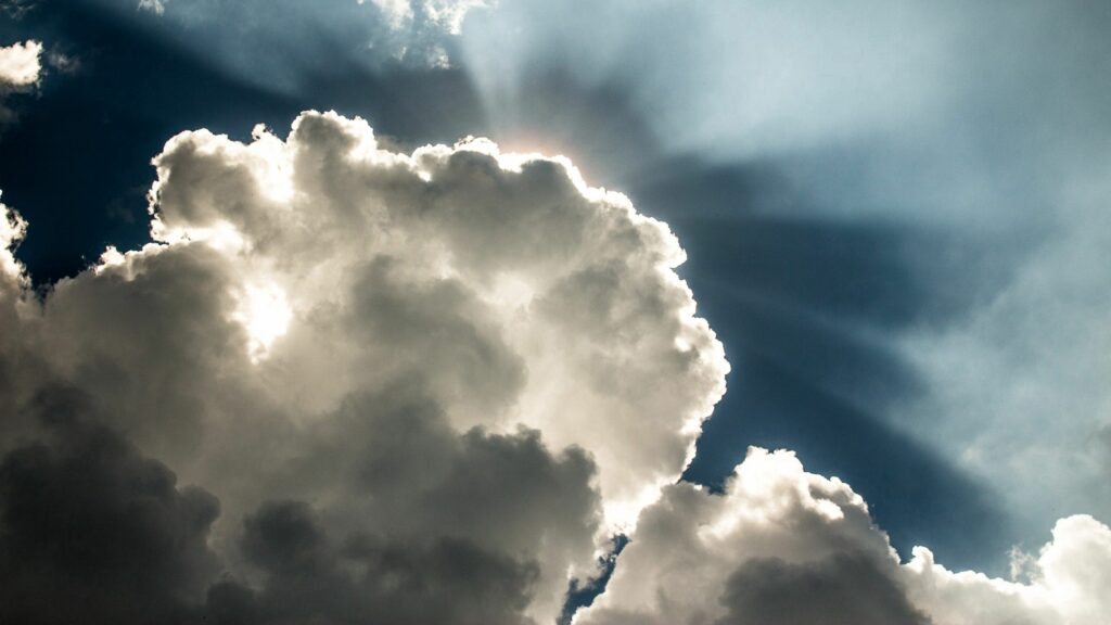 Dramatic sky wallpaper with towering dark and light clouds illuminated by radiant sunlight beams