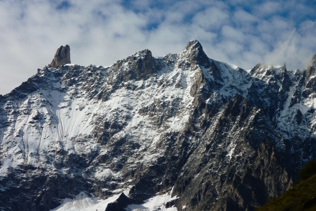 Dramatic snow-capped mountain peaks under partly cloudy sky alpine wilderness wallpaper background