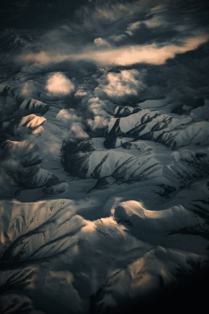 Aerial view of snow-covered rugged mountains with soft sunlight creating shadows and highlights Wallpaper