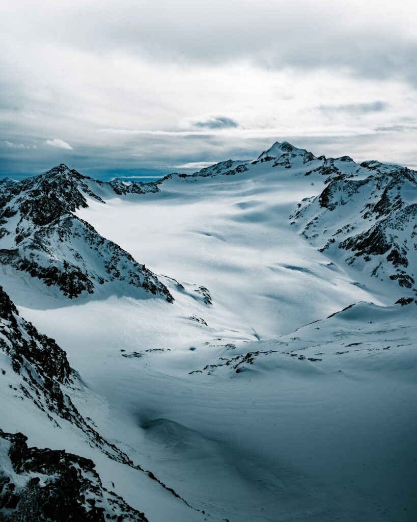 Snow-covered rugged mountain peaks under moody overcast sky winter alpine landscape wallpaper