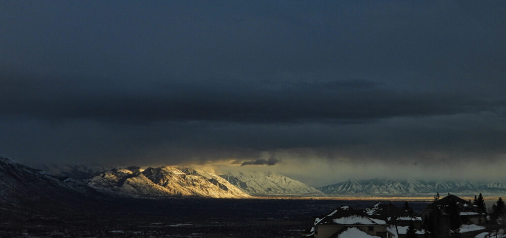 Dramatic snow-capped mountain landscape with deep valley and sunlight breaking through clouds Wallpaper