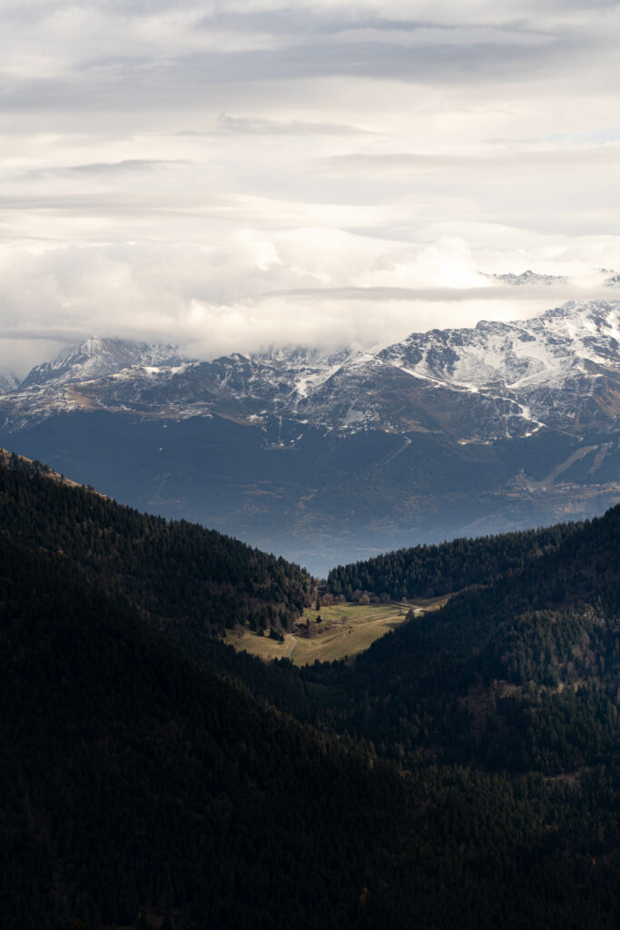 Snowy mountain peaks over dense forests and green valley with dramatic cloud cover wallpaper background