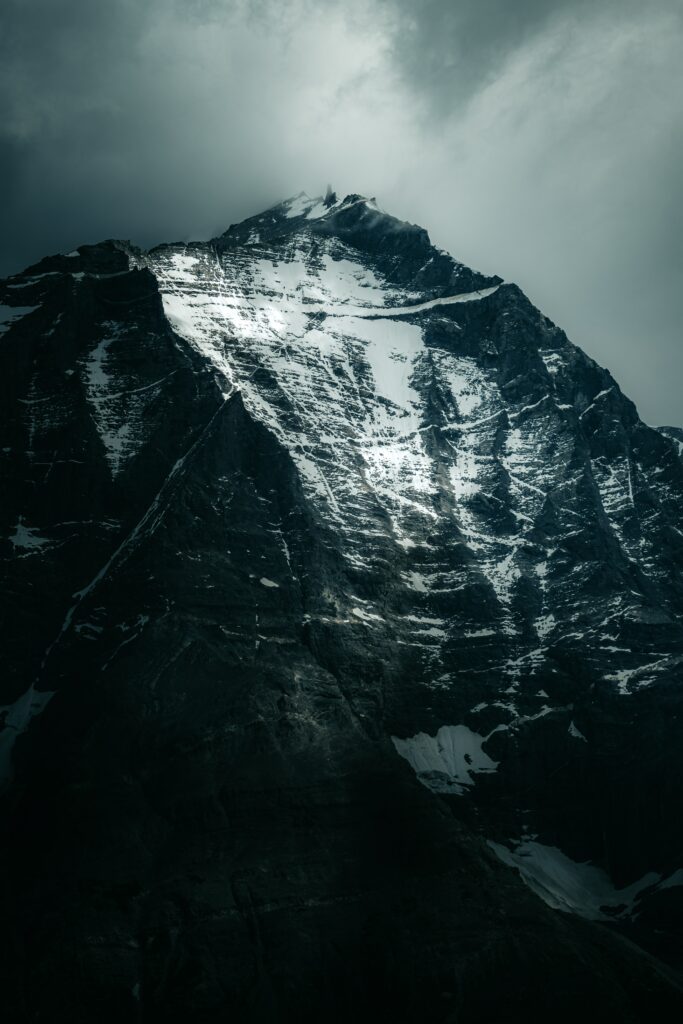 Dramatic mountain peak with snow streaks under stormy sky showcasing rugged rock texture Wallpaper