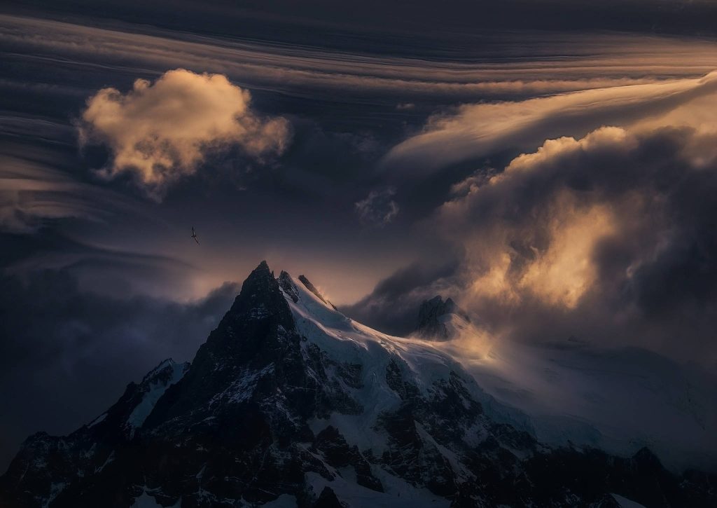 Snow-capped mountain peak at golden twilight with swirling clouds and soaring bird wallpaper