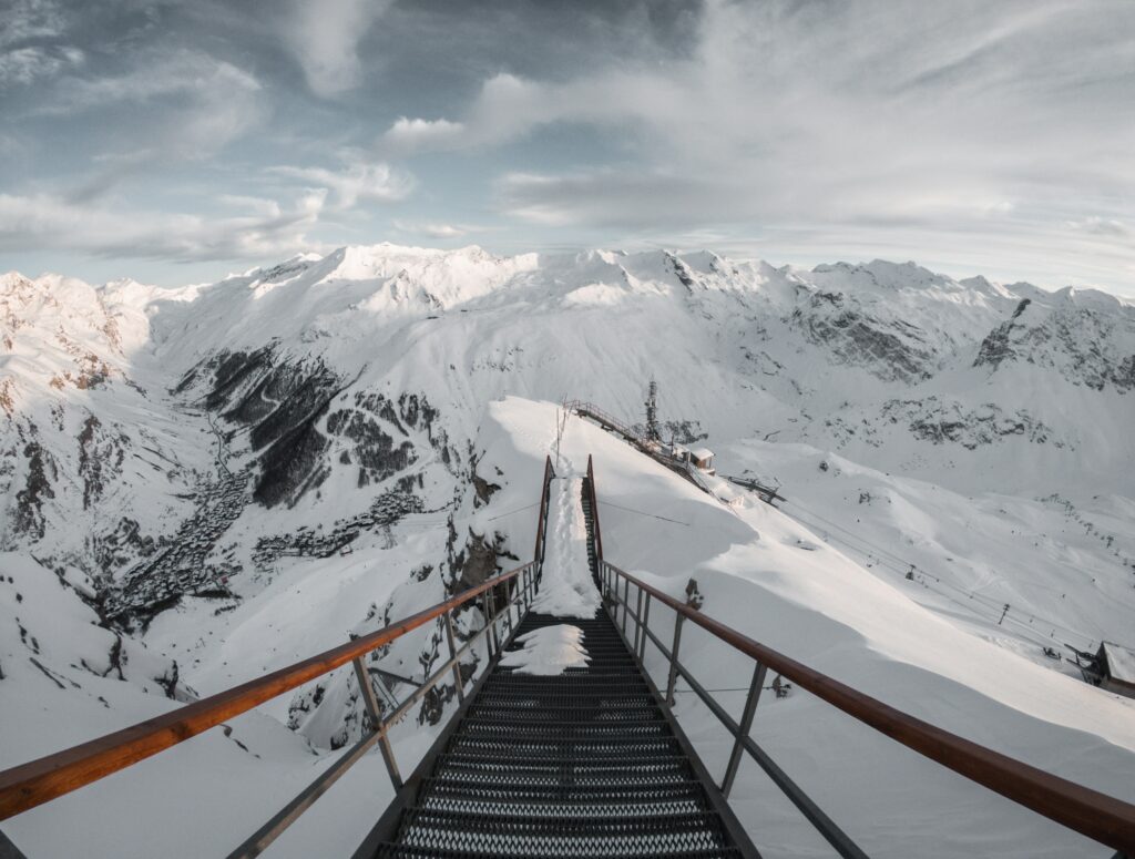 Dramatic bridge over snow-covered alpine mountains under sweeping clouds winter landscape wallpaper